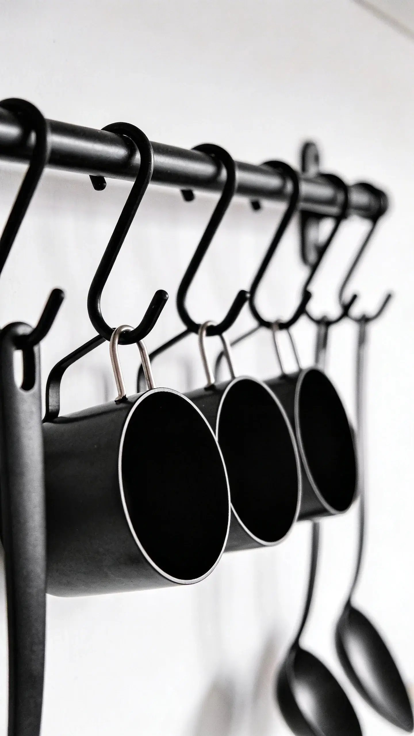 Black rail with S-hooks holding ladles and cups, minimal backdrop