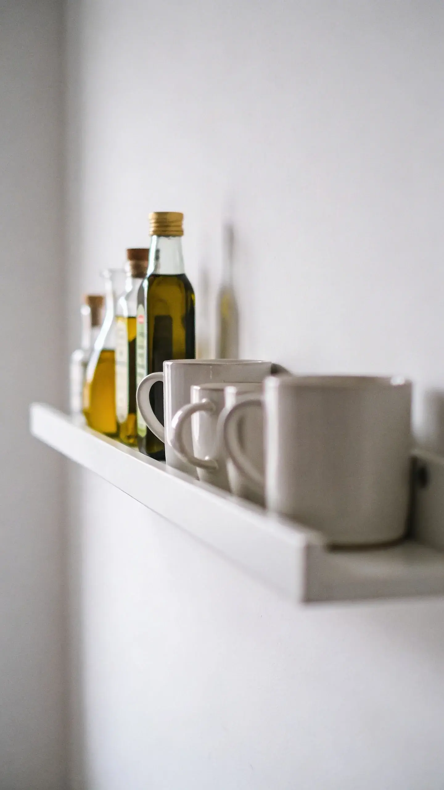 Mugs and oils on narrow floating shelf, clean white wall